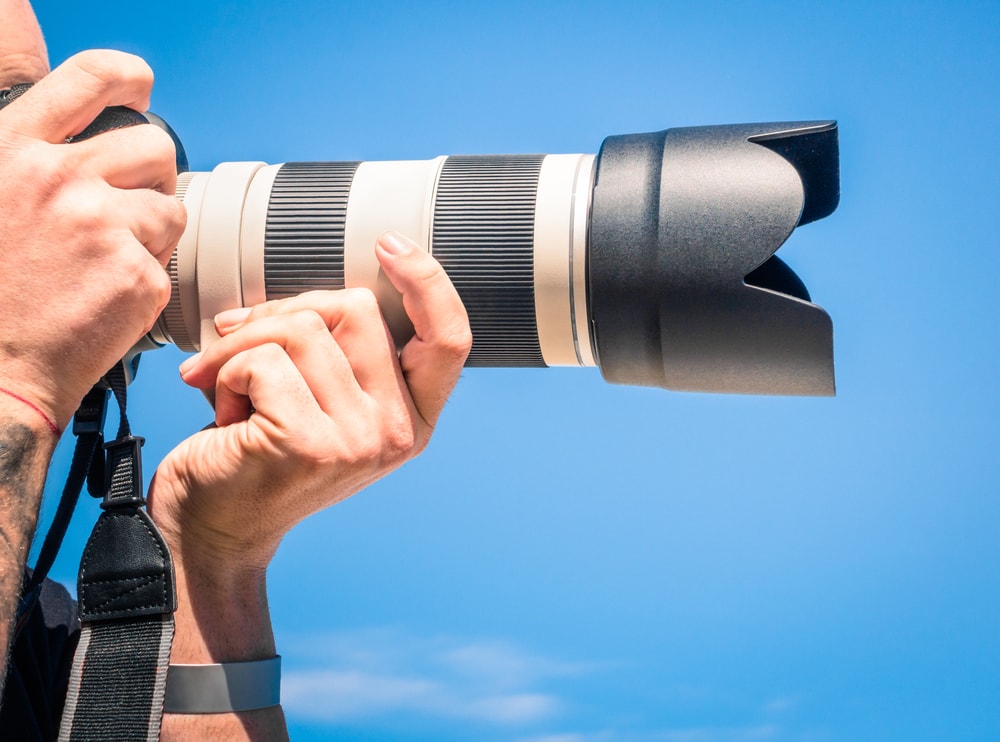 A person holdin a photo camera with long zoom lenses looking at the distance